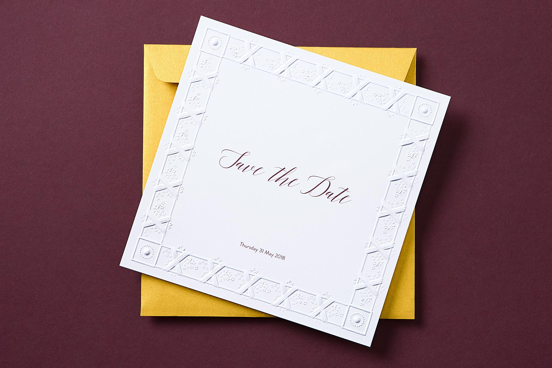 A square white Save the date invitation sits on top of a bright gold envelope