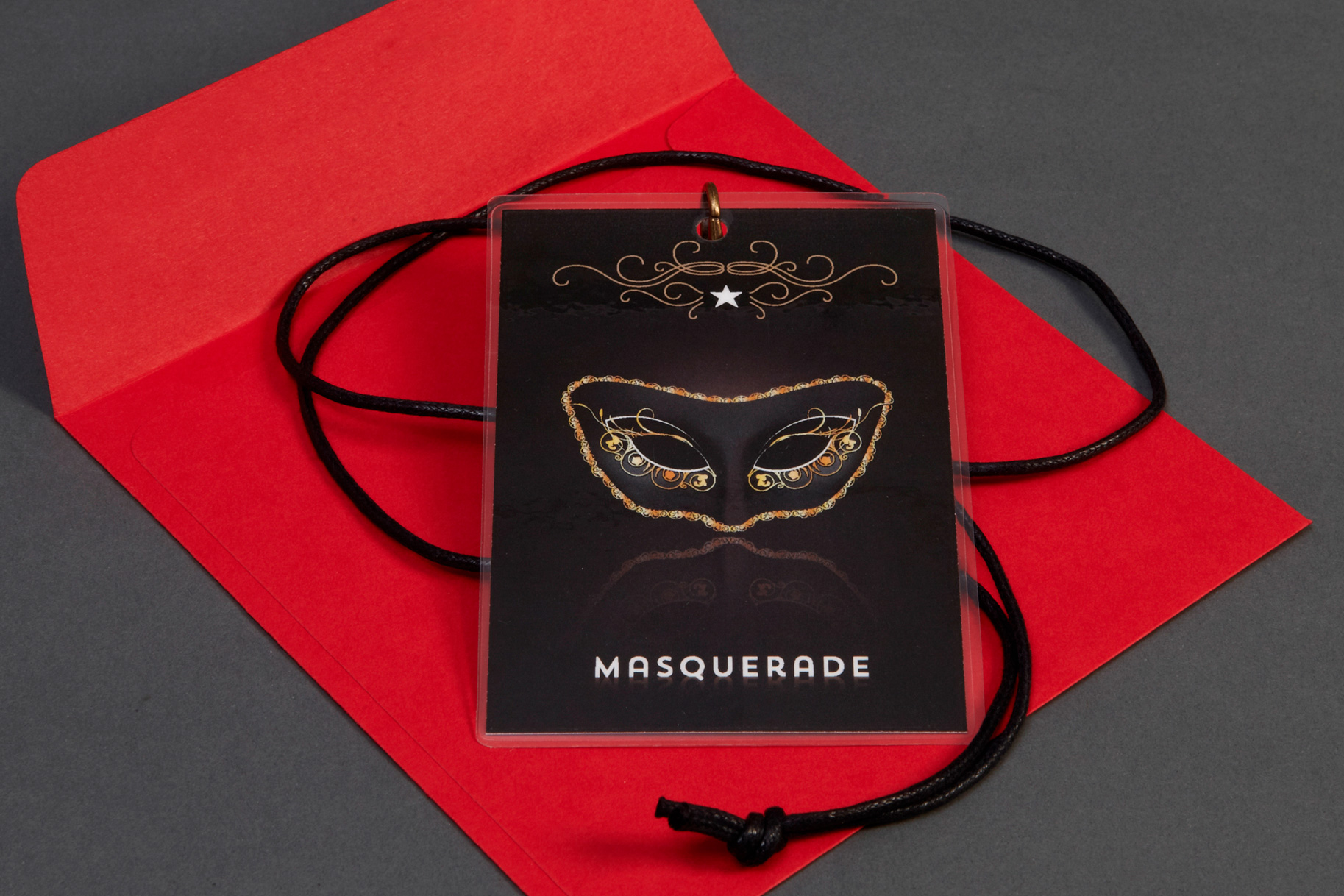 Invitation to a Masquerade party on a leather lanyard, sitting on a red envelope